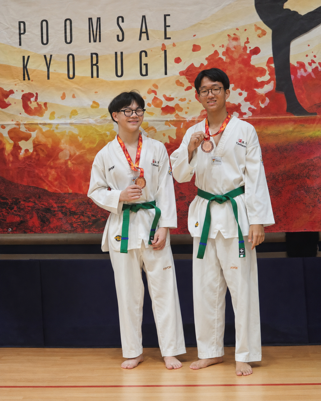 two boys in taekwondo attire stand with medals